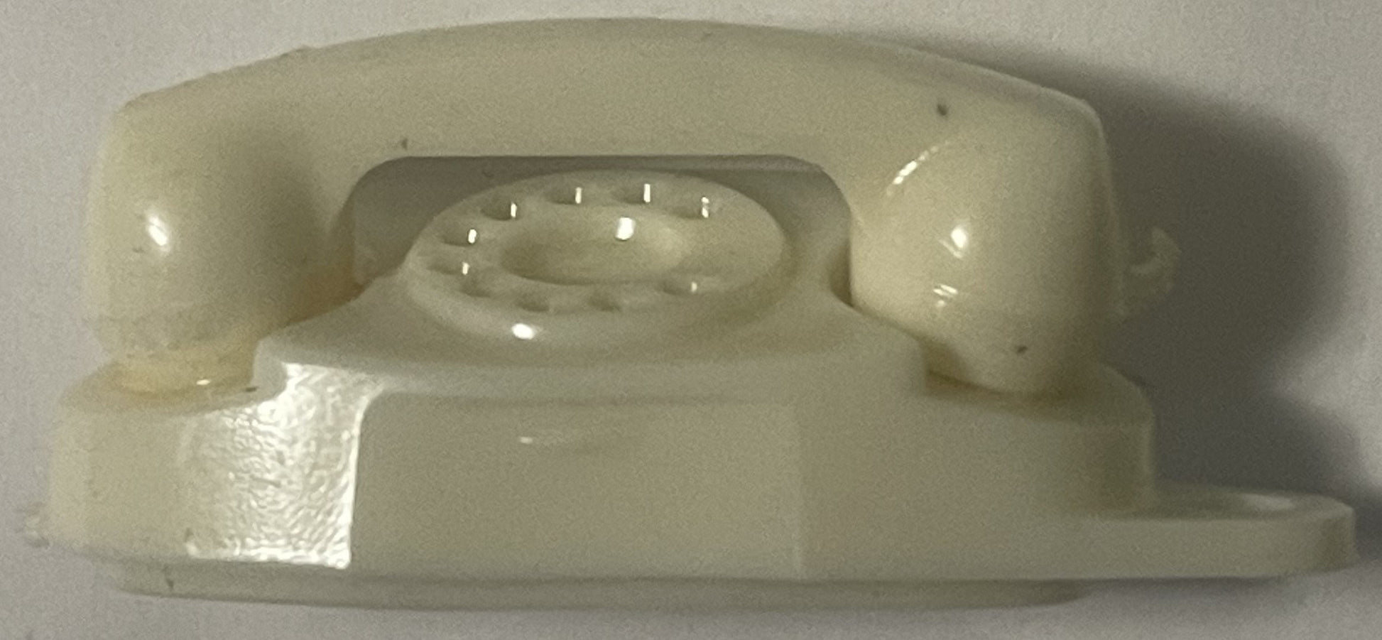 Ivory plastic vintage princess phone keychain shown from above, displaying rotary dial holes and handset details against whit