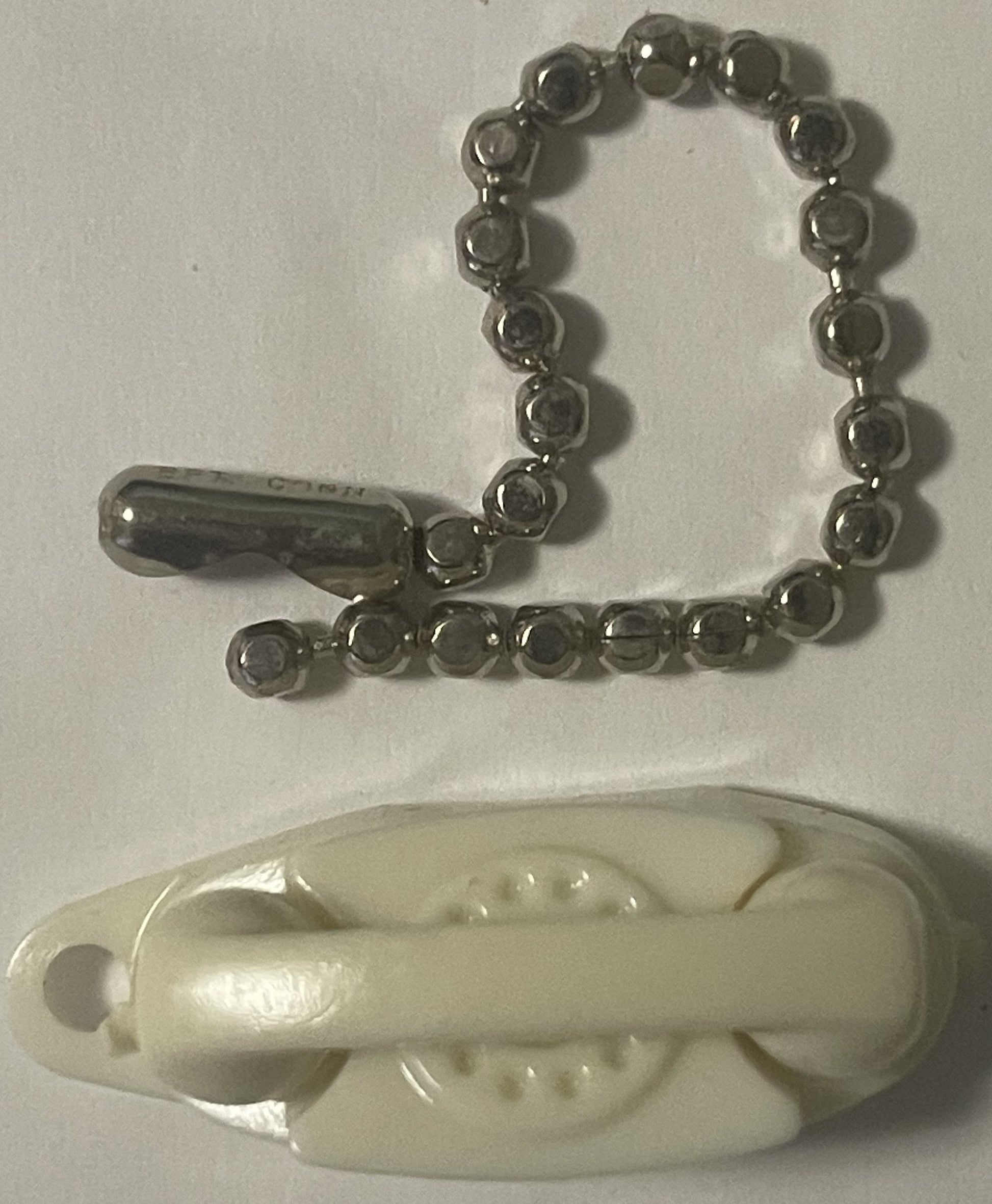 Vintage ivory plastic rotary phone keychain with metal ball chain above cream-colored phone base shown against white backgrou