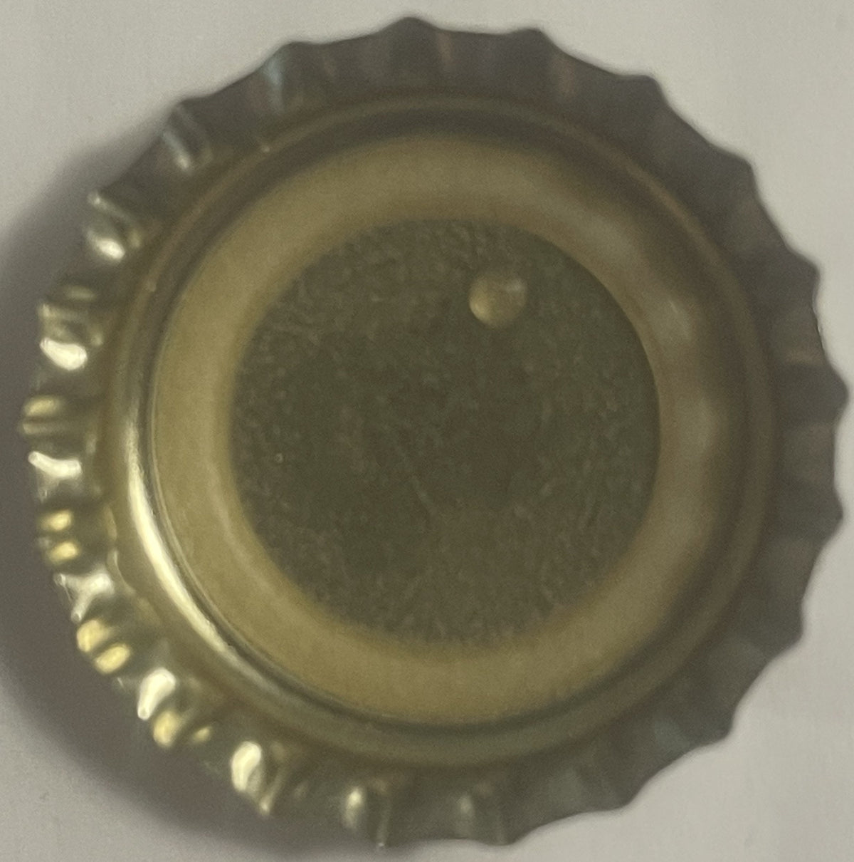 Metallic bottle cap with ridged edges and embossed center disk, shown from above on white background