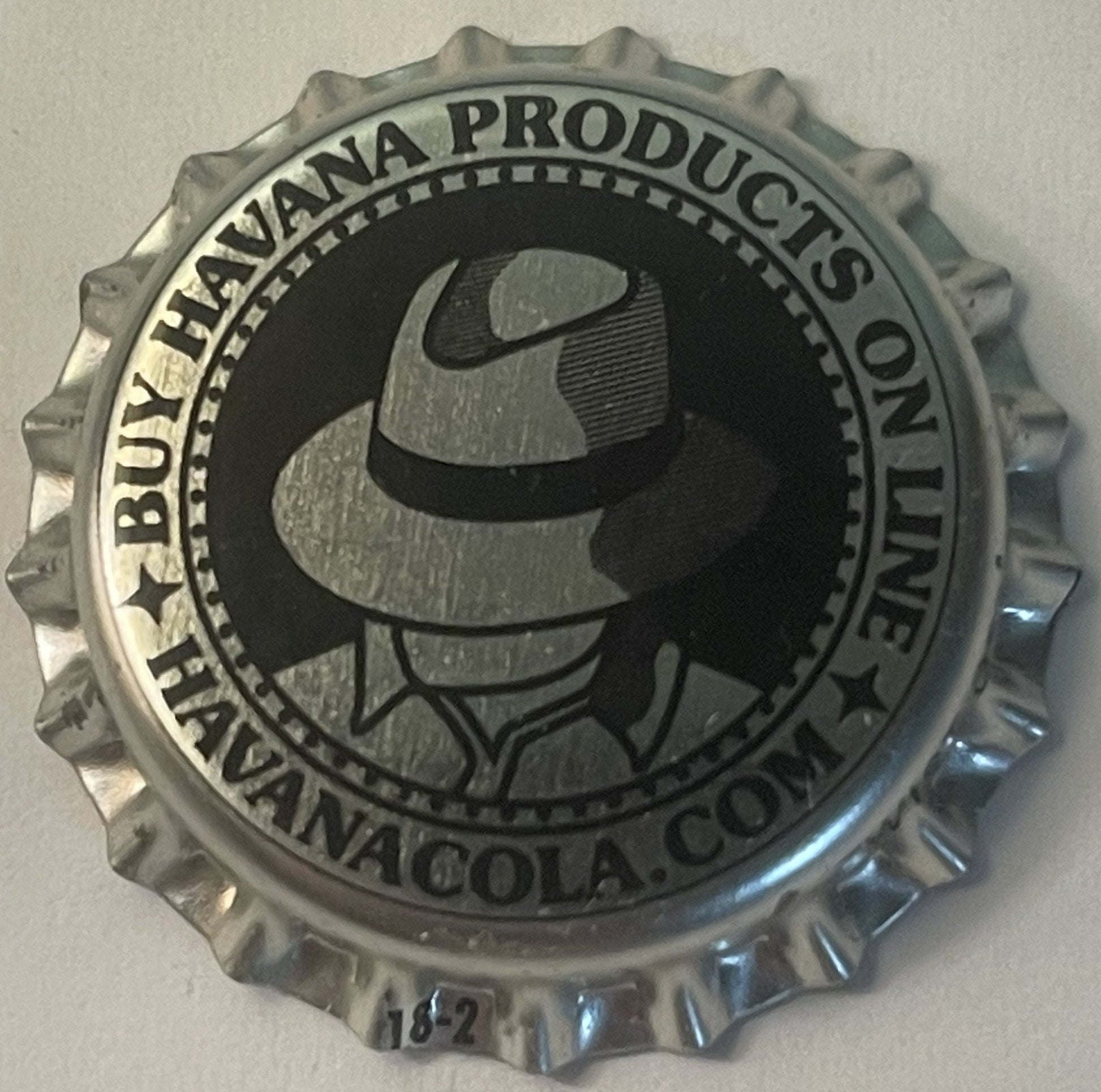 Metallic bottle cap with ridged edges featuring silhouette of man in fedora hat and "Buy Havana Products on Havana Cola, Pens