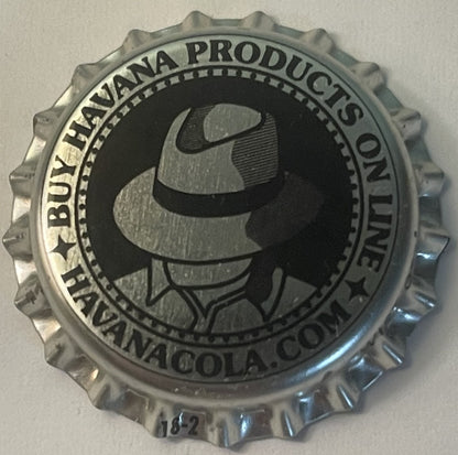 Metallic bottle cap with ridged edges featuring silhouette of man in fedora hat and "Buy Havana Products on Havana Cola, Pens