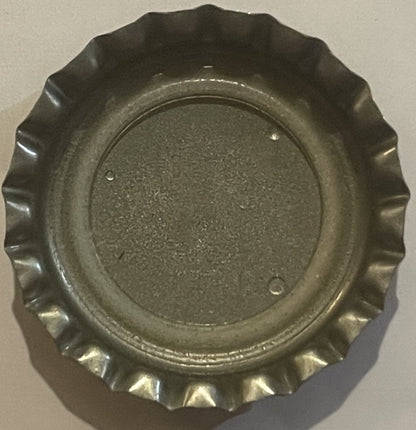 Overhead view of a corrugated metal bottle cap with embossed ridged edges, showing worn metallic finish against a beige backg