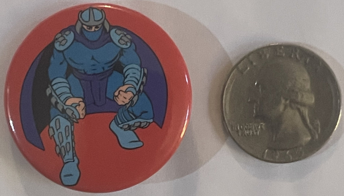 Vintage red circular pin featuring blue armored Shredder character, displayed next to a quarter for scale