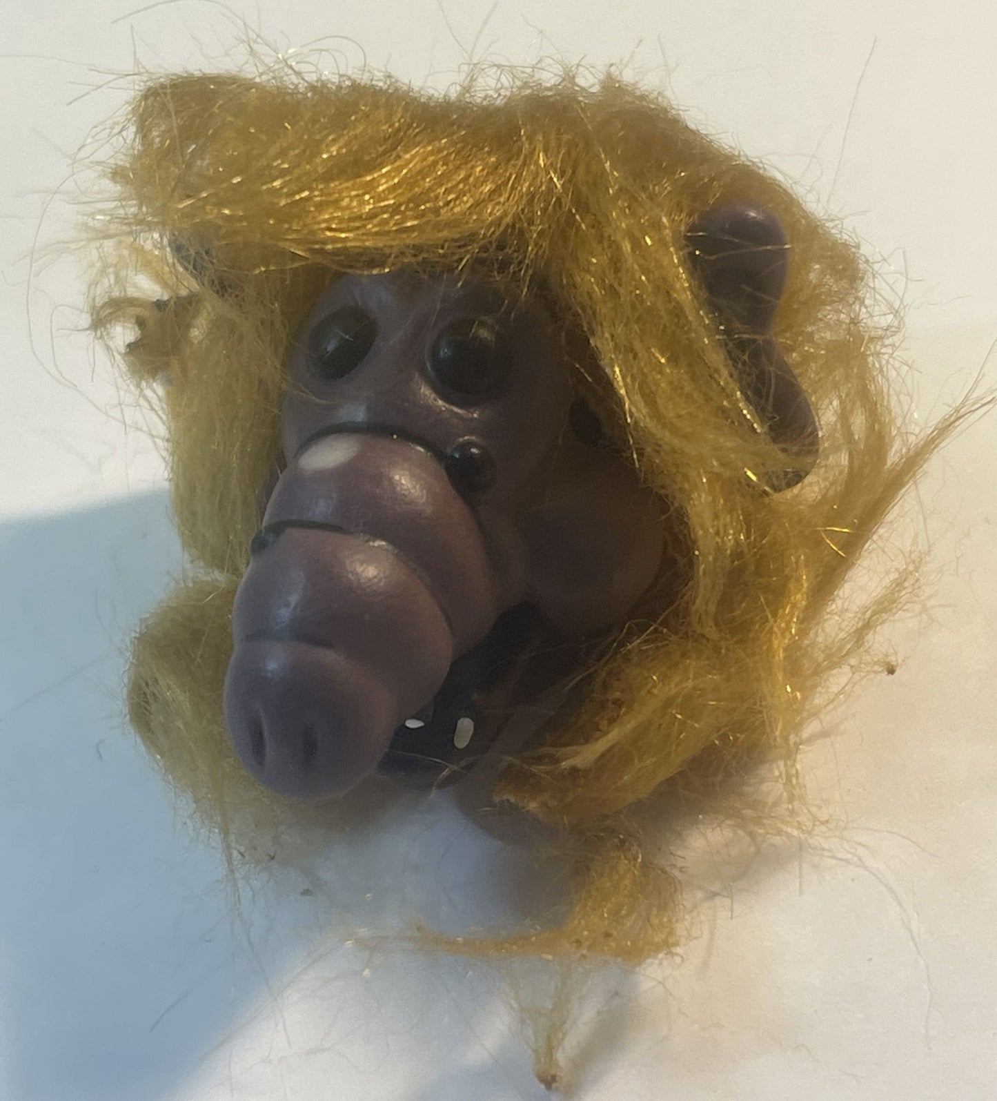 Vintage ALF finger puppet with golden yellow hair, dark rubber face, and prominent nose, shown in close-up against a light ba