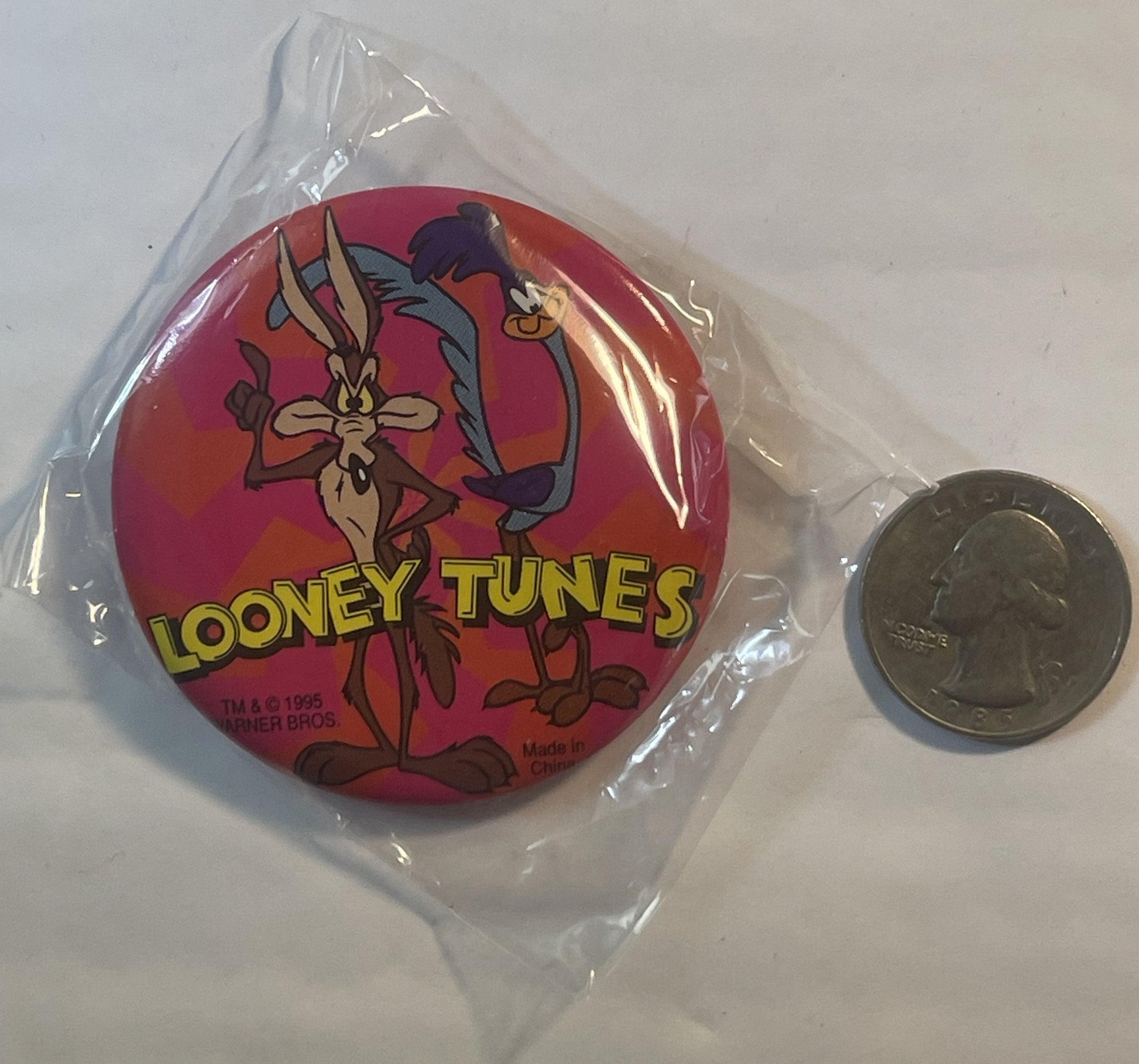 Sealed vintage Looney Tunes pin featuring Wile E. Coyote and Roadrunner on red background, shown next to quarter for scale