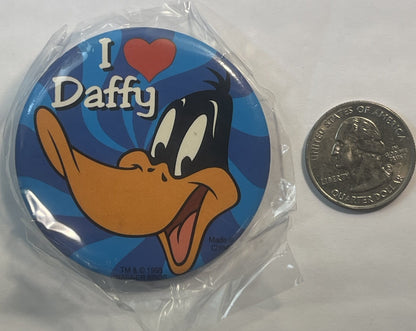 Unopened 1995 Daffy Duck pin in plastic wrapper next to a quarter for scale, showing cartoon duck with "I ♥ Daffy" text on bl