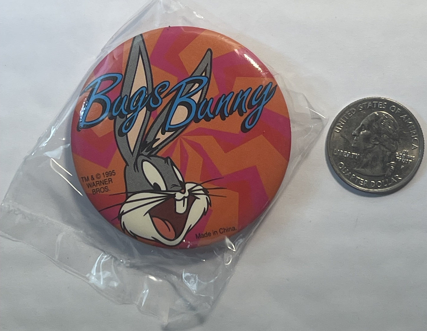 Vintage Bugs Bunny pin in clear plastic packaging next to a quarter for scale, showing colorful red and orange geometric back