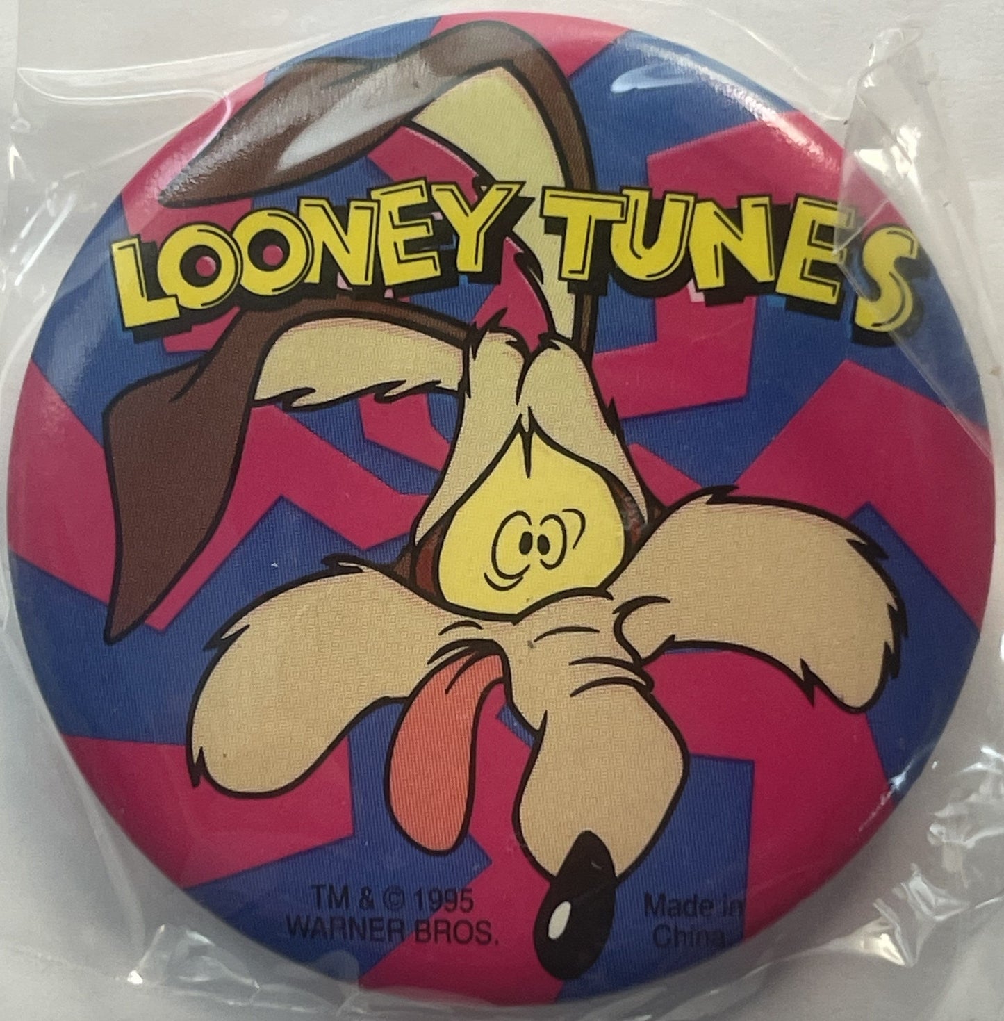 Circular pin featuring cartoon character Wile E. Coyote in tan and brown on red and blue checkered background, "LOONEY TUNES"
