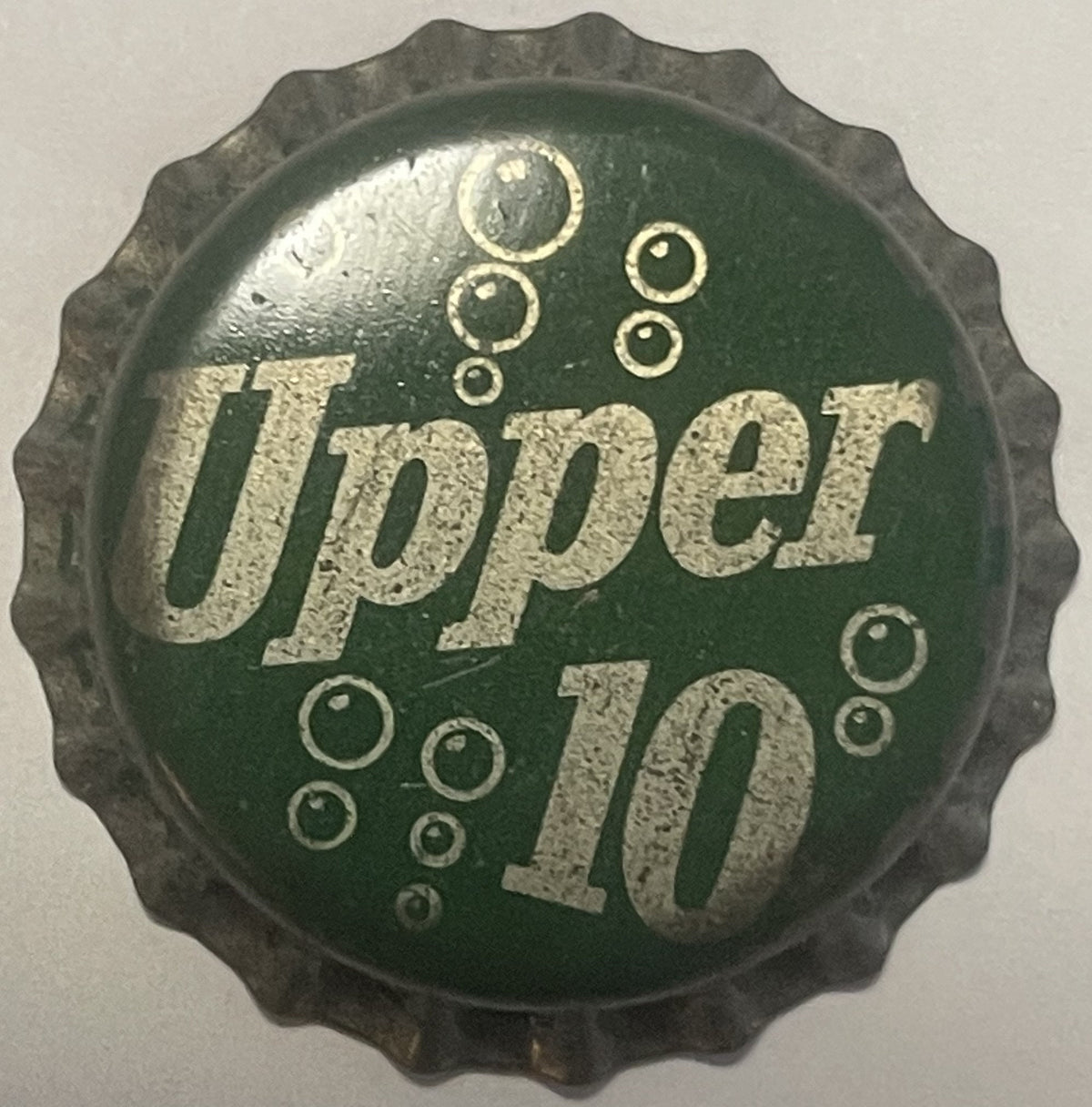 Vintage green and silver Upper 10 cork bottle cap with embossed bubbles and text, photographed flat against light background