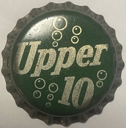 Vintage green and silver Upper 10 cork bottle cap with embossed bubbles and text, photographed flat against light background