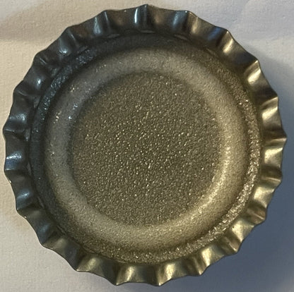 Overhead view of a metal bottle cap with crimped edges and textured surface, showing wear consistent with vintage