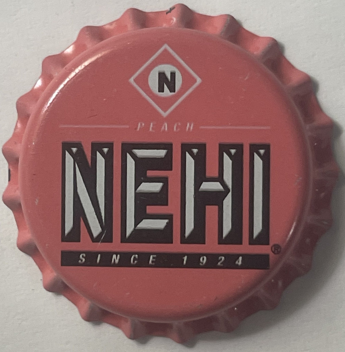 Vintage Nehi peach bottle cap with corrugated edges, showing diamond-shaped "N" logo, "NEHI" text, "PEACH" and "SINCE 1924" p