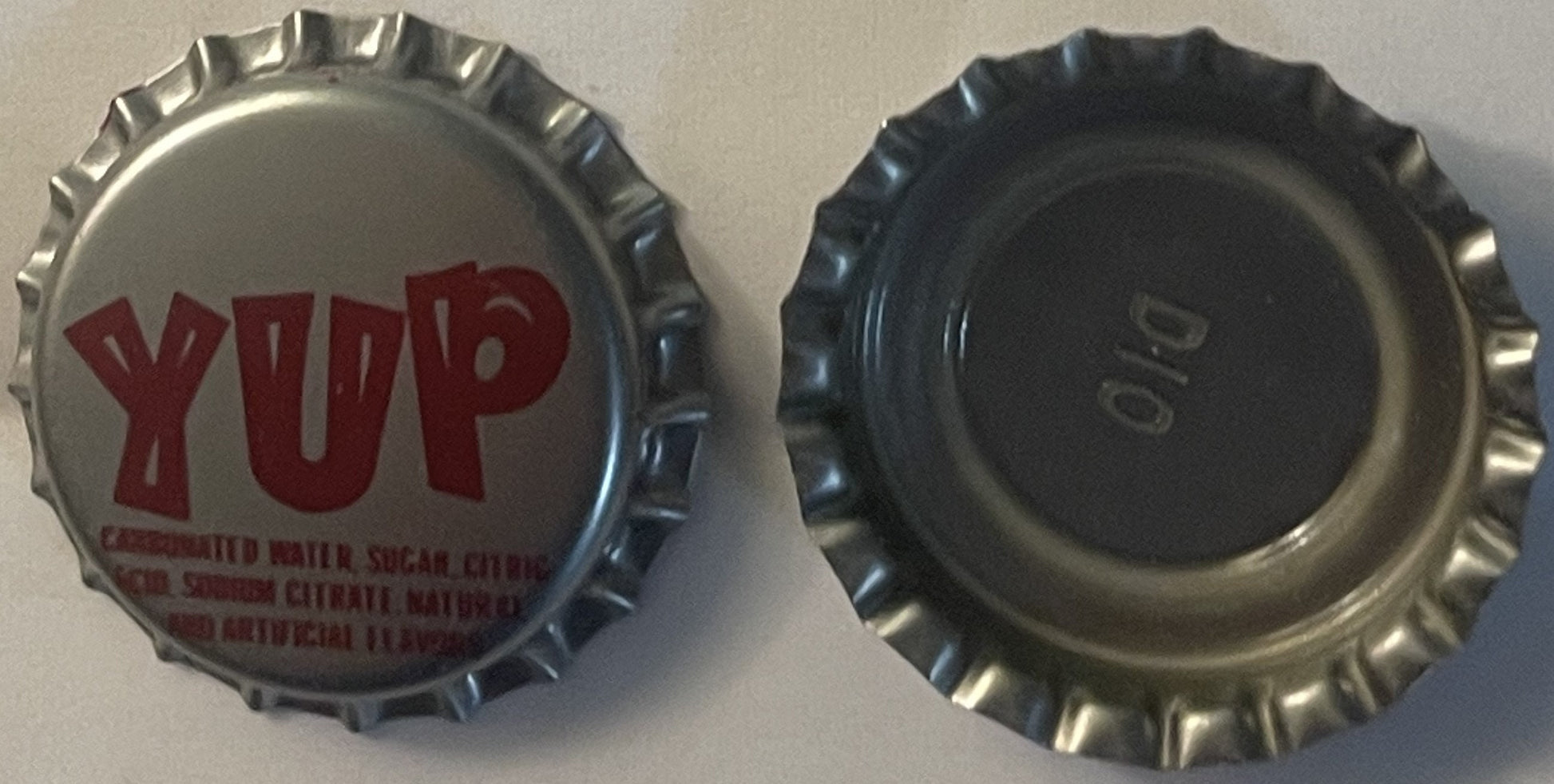 Vintage YUP soda bottle cap showing front with red text and back side, both displayed against tan background