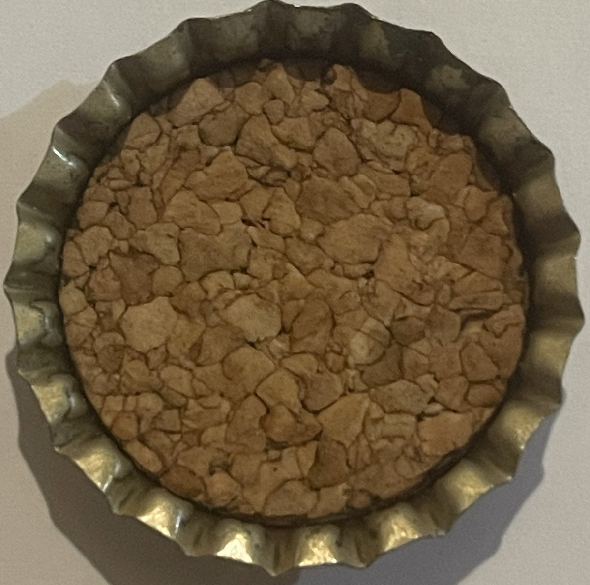 Vintage bottle cap with corrugated metal rim and tan cork-lined interior, viewed from above on white surface