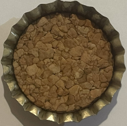 Vintage bottle cap with corrugated metal rim and tan cork-lined interior, viewed from above on white surface