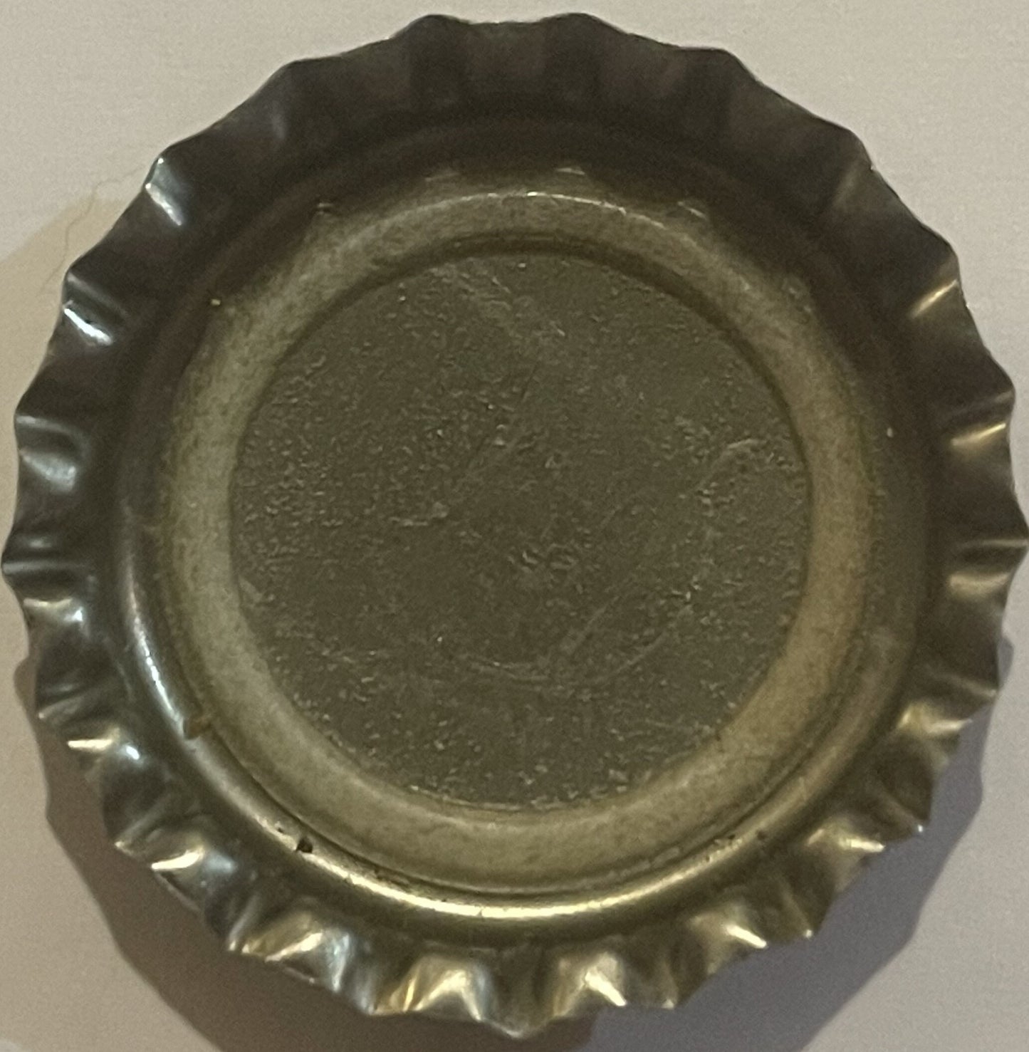 Overhead view of a vintage metal bottle cap with crimped ridged edges, showing embossed circular center design on dark metall