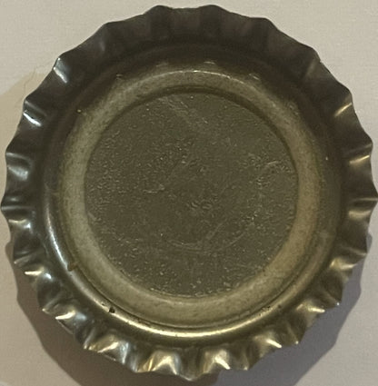 Overhead view of a vintage metal bottle cap with crimped ridged edges, showing embossed circular center design on dark metall