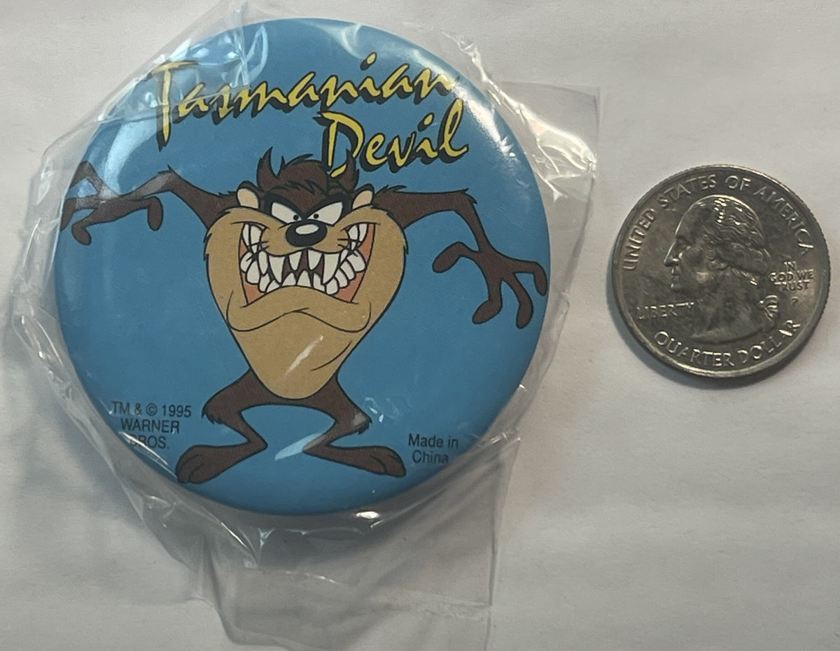 Circular blue pin featuring angry Tasmanian Devil character with text "Tasmanian Devil" and Warner Bros copyright 1995, shown