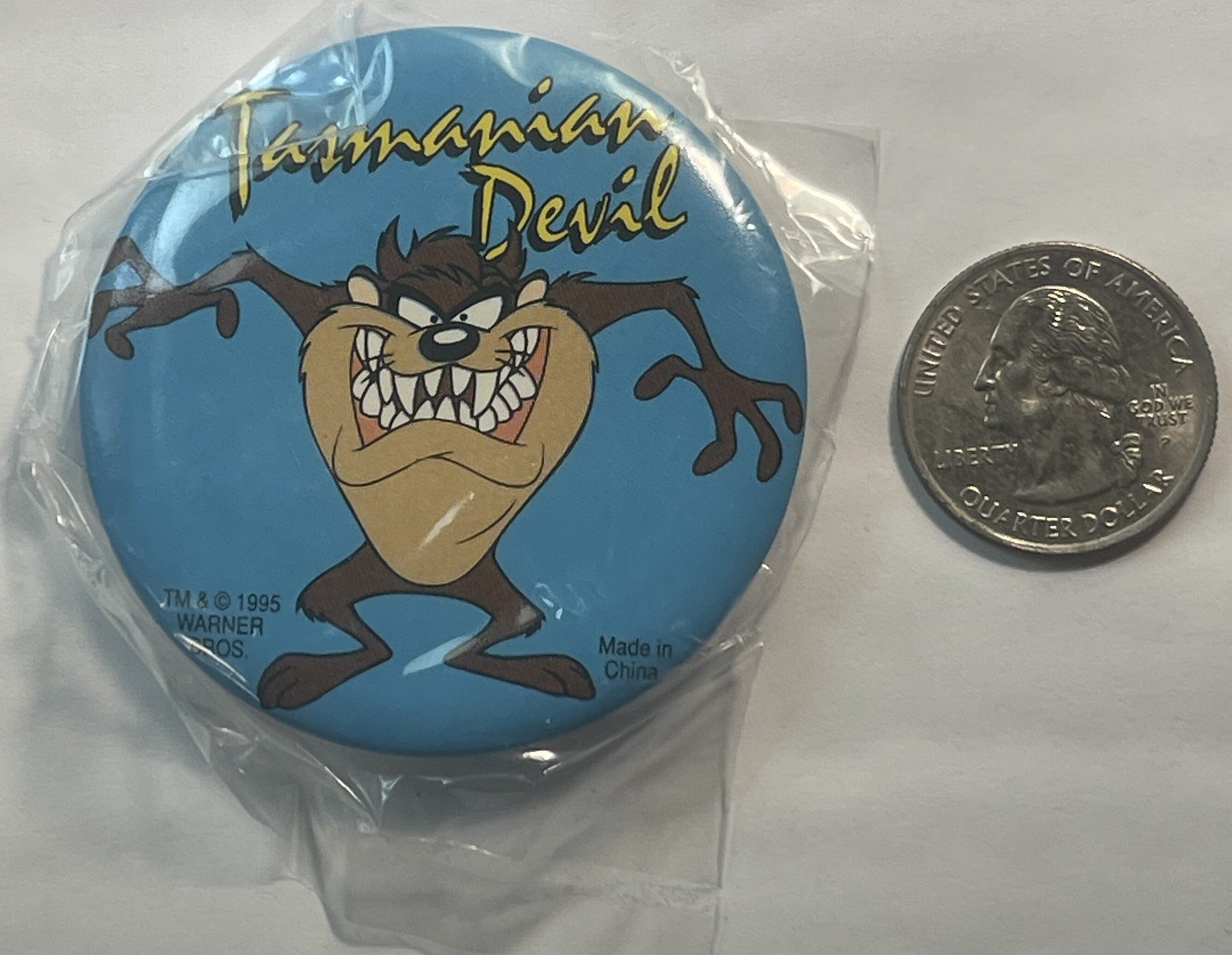 Circular blue pin featuring angry Tasmanian Devil character with text "Tasmanian Devil" and Warner Bros copyright 1995, shown