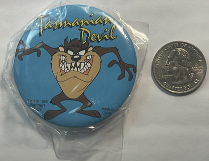 Circular blue pin featuring angry Tasmanian Devil character with text "Tasmanian Devil" and Warner Bros copyright 1995, shown