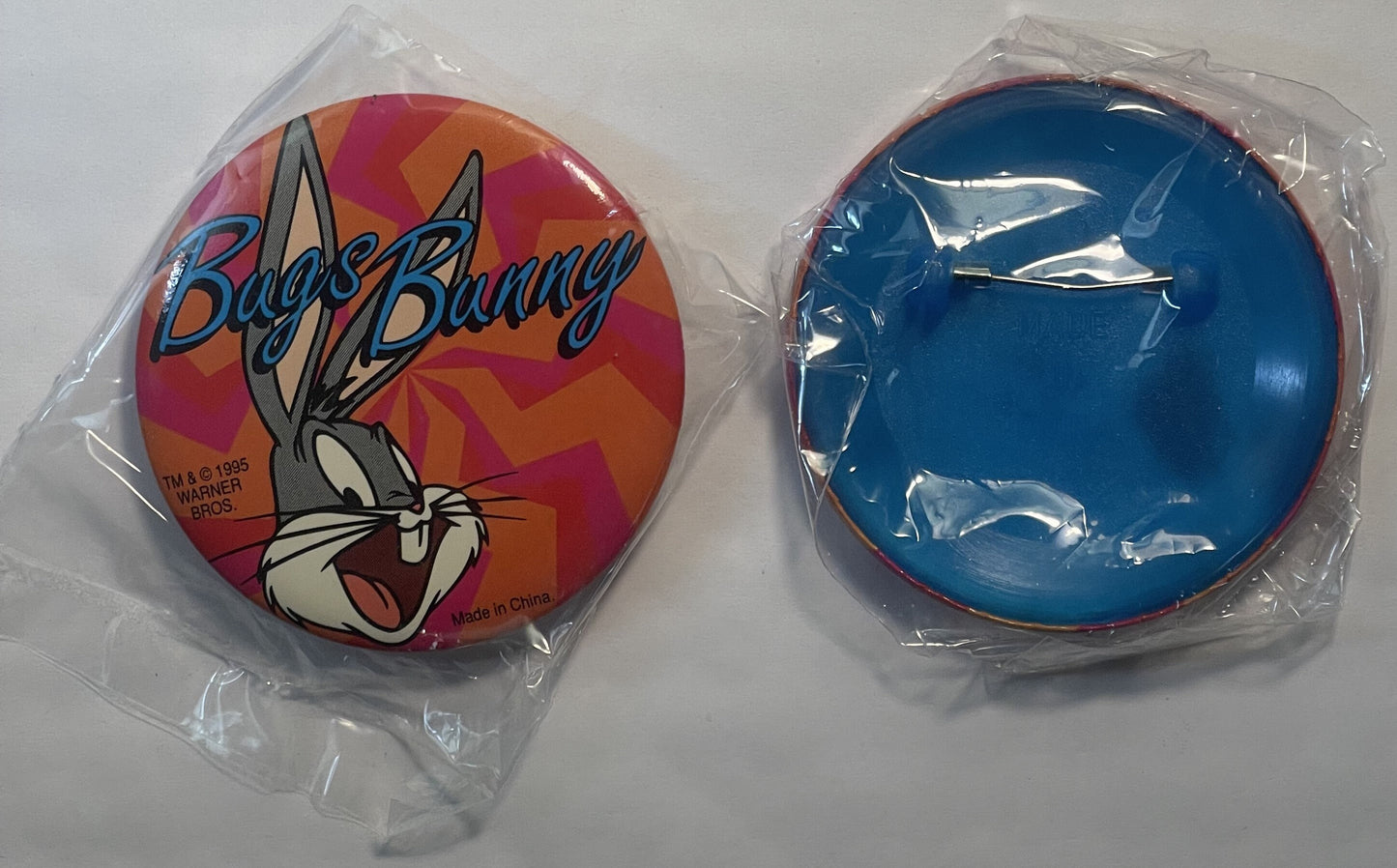 Two circular pins in plastic packaging shown front and back: colorful Bugs Bunny character design with red and orange backgro