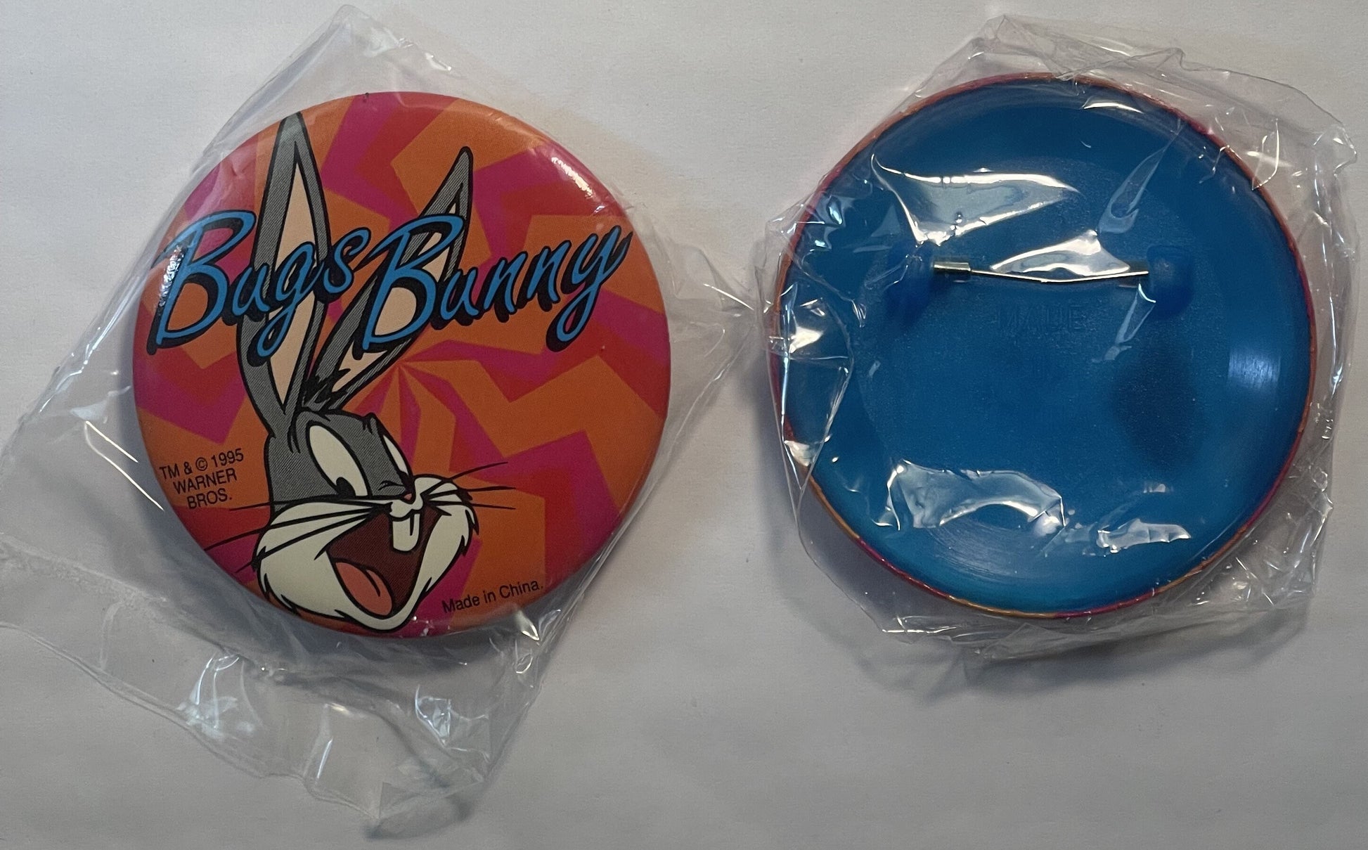 Two circular pins in plastic packaging shown front and back: colorful Bugs Bunny character design with red and orange backgro