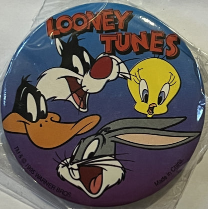 Circular Looney Tunes pin featuring Bugs Bunny, Daffy Duck, and Tweety Bird on blue-to-purple gradient background, still seal