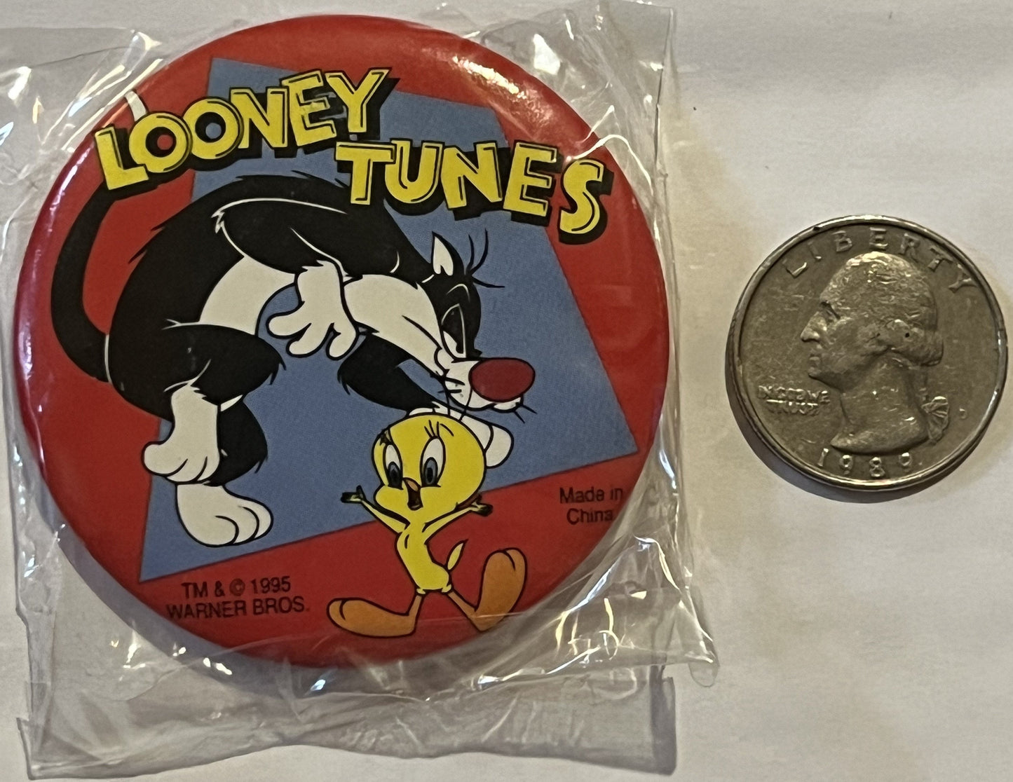 Unopened 1995 Warner Bros Looney Tunes pin featuring Sylvester and Tweety in plastic packaging, shown next to a quarter for s