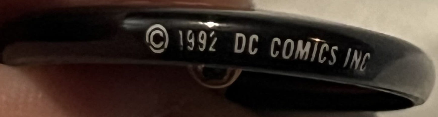 Close-up of black pinback button rim showing embossed text "© 1992 DC COMICS INC