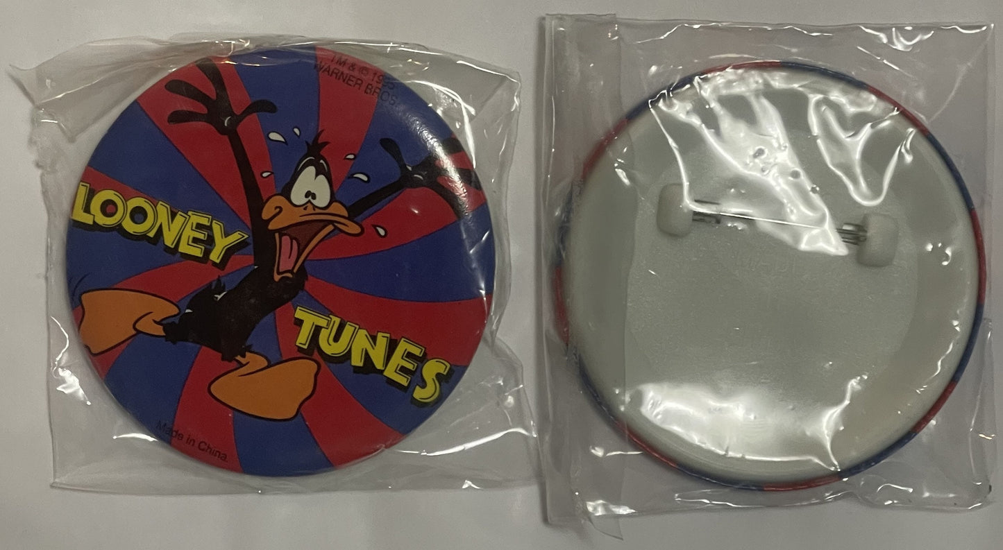 Two circular pins in plastic packaging showing Daffy Duck character on front with "LOONEY TUNES" text, blank back side visibl