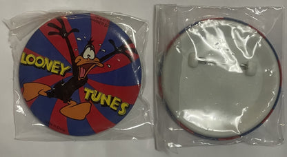Two circular pins in plastic packaging showing Daffy Duck character on front with "LOONEY TUNES" text, blank back side visibl