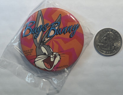 Unopened circular Bugs Bunny pin with colorful geometric background, displayed next to a quarter for scale, showing Warner Br