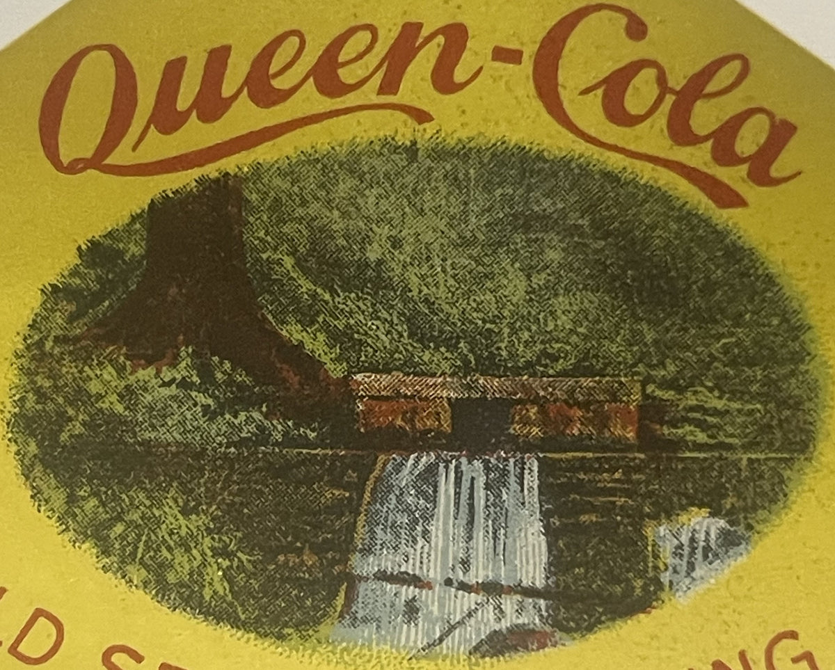 Vintage Queen Cola bottle label with yellow background, brown script text, and central oval image of a log cabin