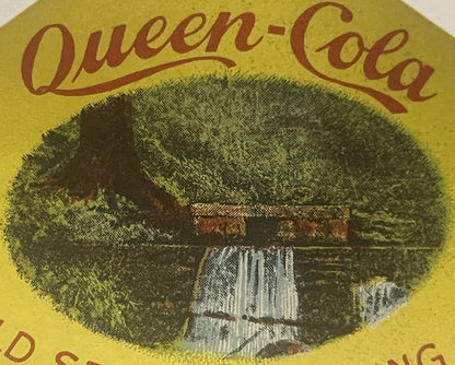 Vintage Queen Cola bottle label with yellow background, brown script text, and central oval image of a log cabin