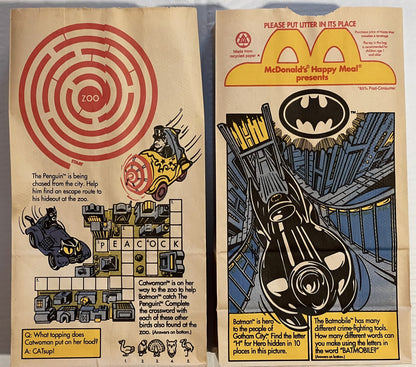 Two vintage McDonald's Happy Meal paper bags with Batman and Penguin DC Comics characters, games, and puzzles printed in red,