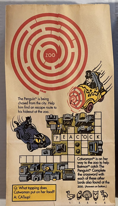 Vintage McDonald's Happy Meal bag featuring Batman characters, maze puzzle, and crossword game with red spiral design on crea