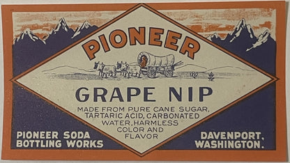 Vintage Pioneer Grape Nip soda label from Davenport, Washington, featuring mountains, covered wagon, and brown/cream diamond-