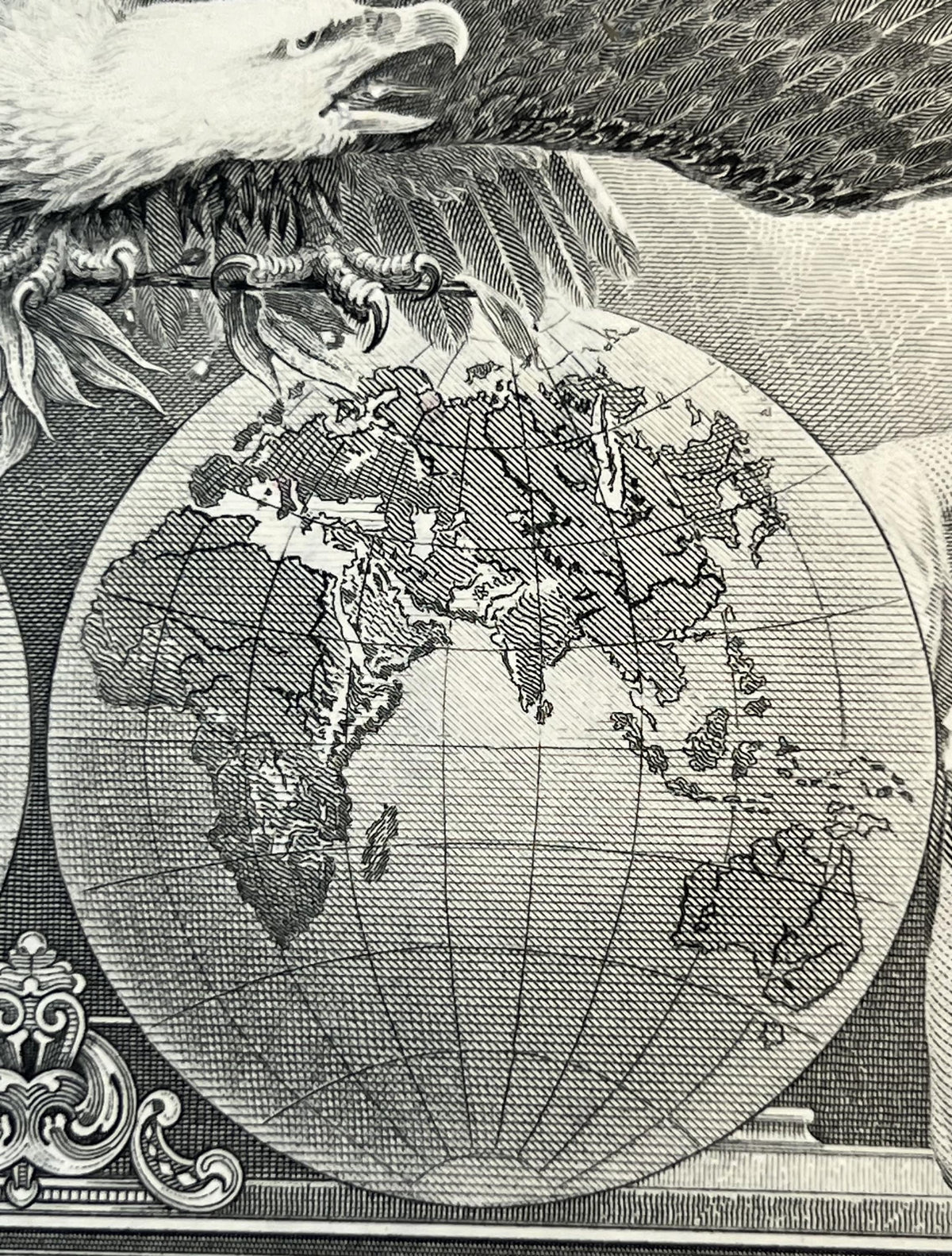 Black and white engraved map showing North America and surrounding continents held by an eagle, with ornamental cartouche det
