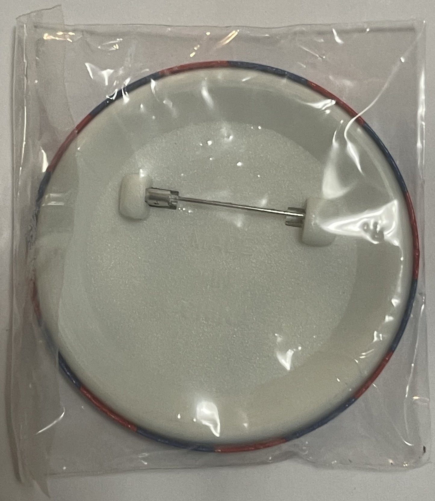 Sealed plastic package containing a circular pin with red and blue wire attachment and metal clasp, mounted on white foam bac