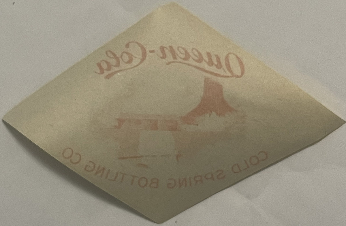 Cream-colored vintage label rotated at diamond angle, embossed with "Queen-1990" at top, silhouette of building in center