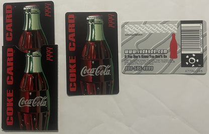Three vintage Coca-Cola promotional cards from 1999 displayed flat: two black accordion-fold cards showing bottle imagery and