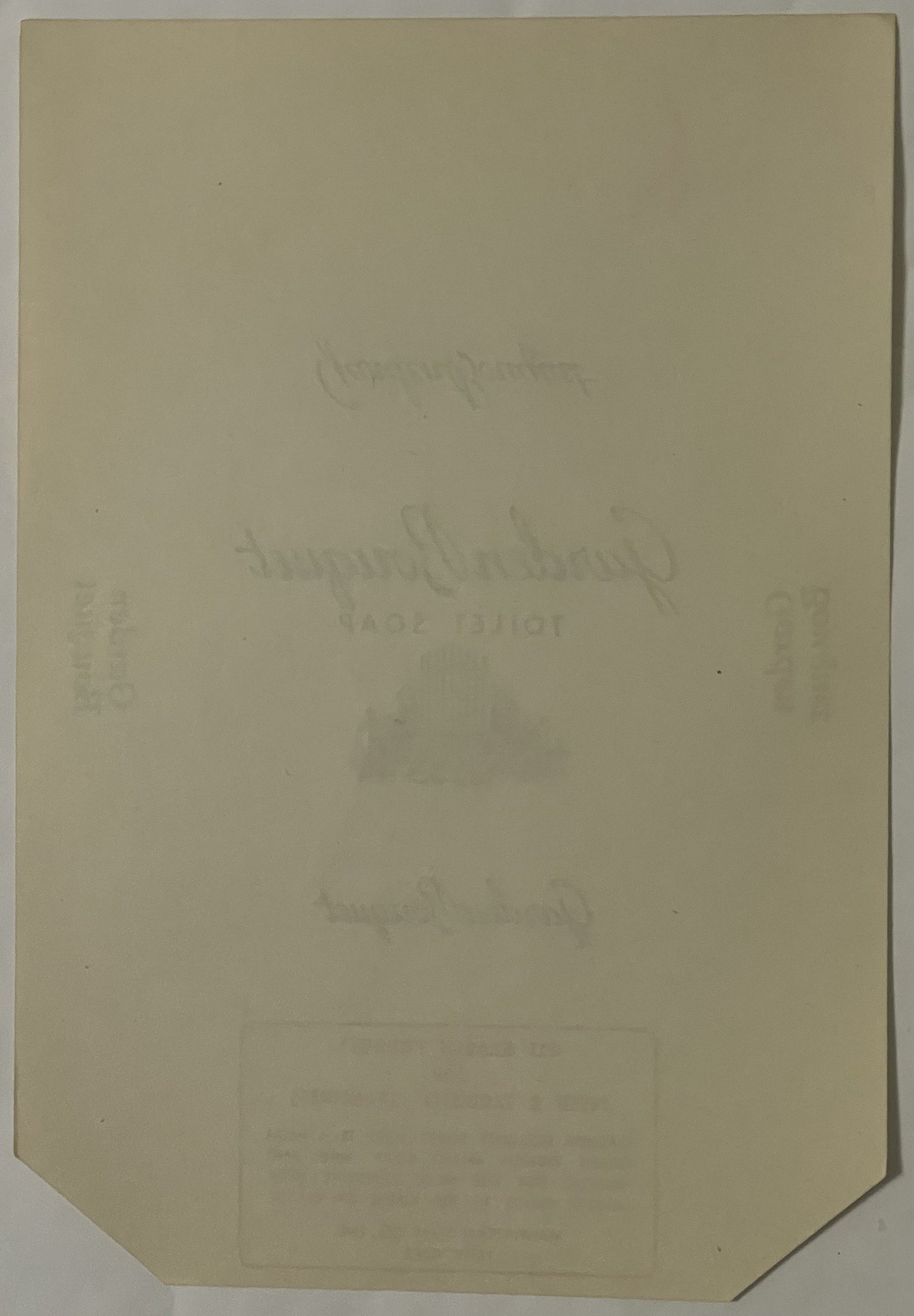 Cream-colored antique soap label with faint embossed text, angled to show corner detail, photographed flat against neutral ba