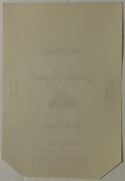 Cream-colored antique soap label with faint embossed text, angled to show corner detail, photographed flat against neutral ba