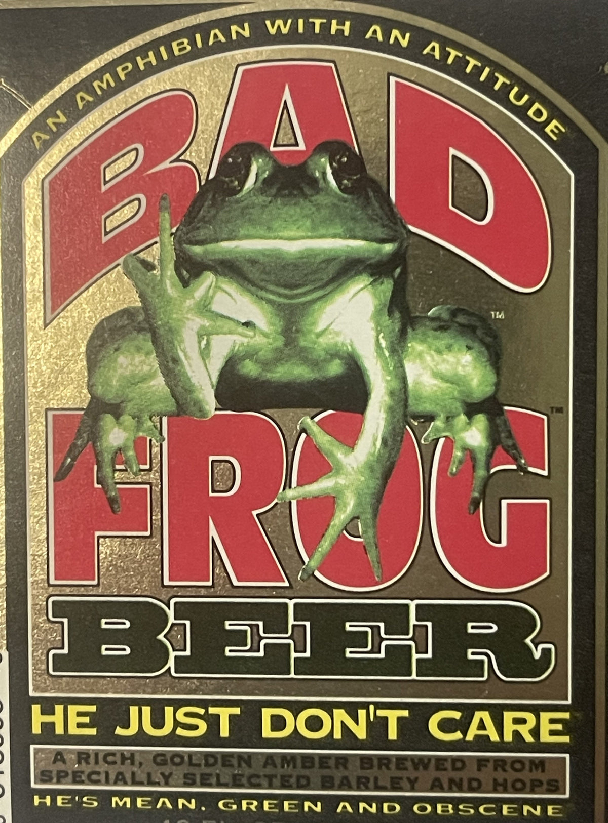 Vintage Bad Frog Beer label with green frog illustration, red text, gold border, and tagline "He Just Don't Care" on dark