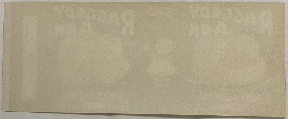 Faded cream-colored vintage can label with barely visible Raggedy Ann imagery and text, photographed flat against white backg
