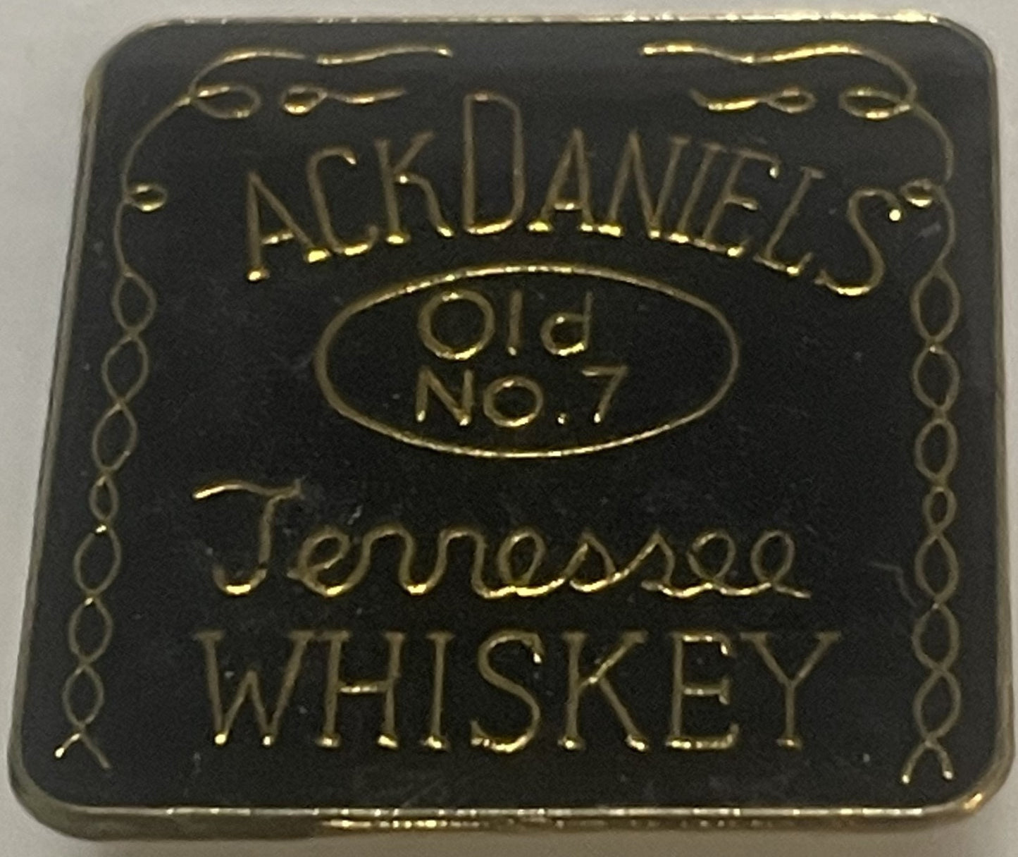 Square black enamel pin with gold embossed Jack Daniel's Old No. 7 Tennessee Whiskey branding and decorative border, shown fl