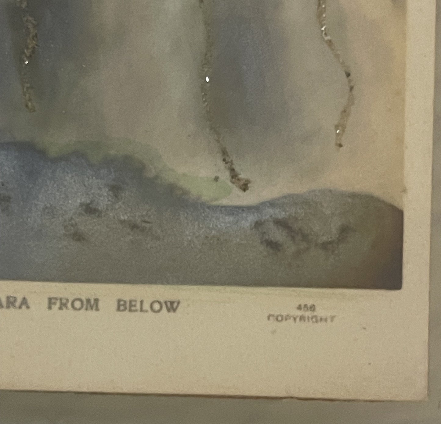 Aged postcard corner showing "FROM BELOW" text and copyright mark, with water-stained vintage photograph of Niagara Falls abo