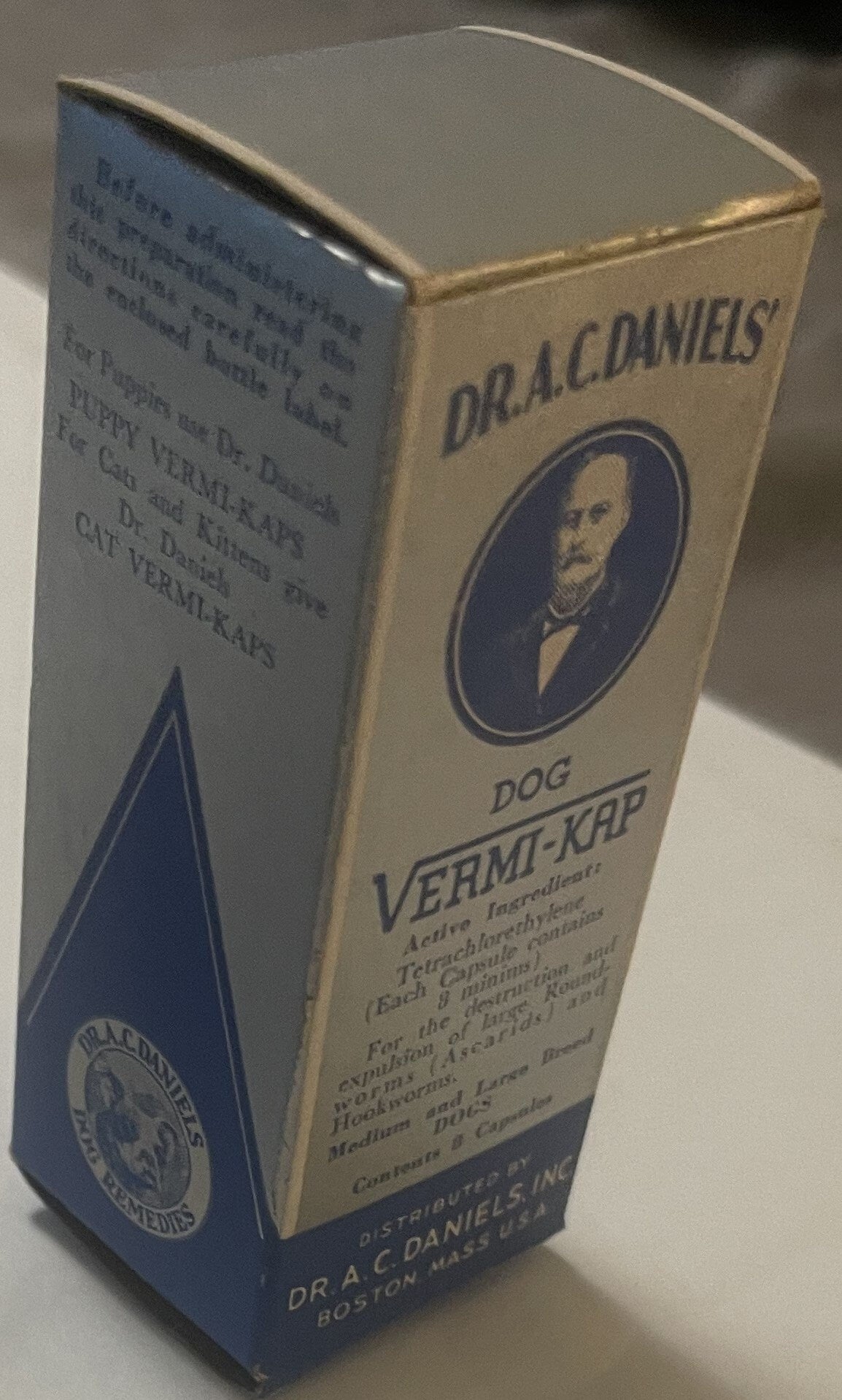 Cream and navy cardboard box for Dr. A.C. Daniels Dog Vermi-Kap medicine, showing portrait medallion and text, photographed