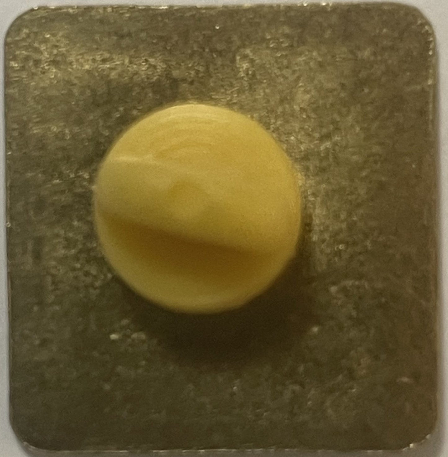 Cream-colored round enamel pin on gray textured backing card, shown from above