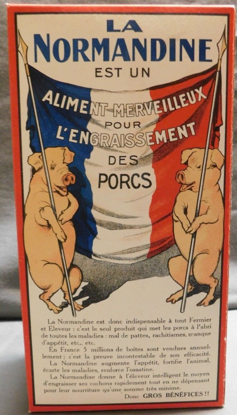 La Normandine box folded and standing, back panel: two pigs holding a French tricolor flag lettered ALIMENT MERVEILLEUX POUR L'ENGRAISSEMENT DES PORCS, red-bordered sales text below